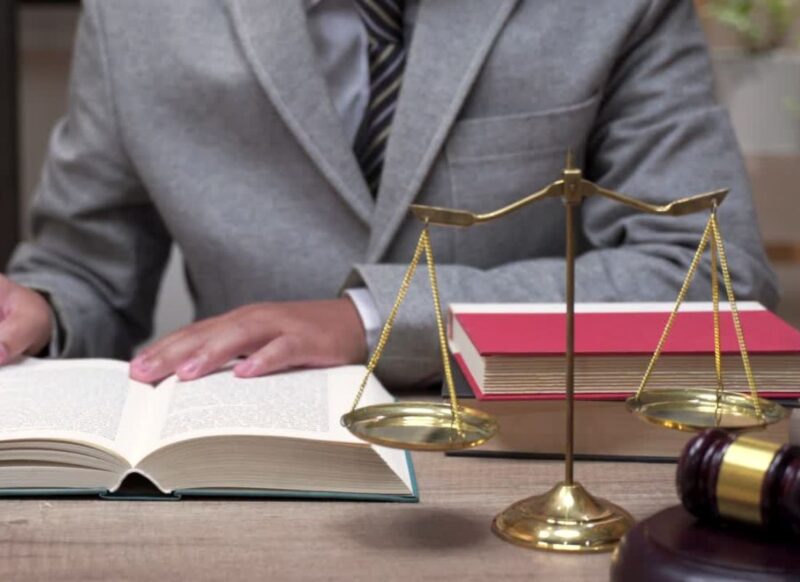 advokat čita knjigu, pored njega advokatska vagica i palica