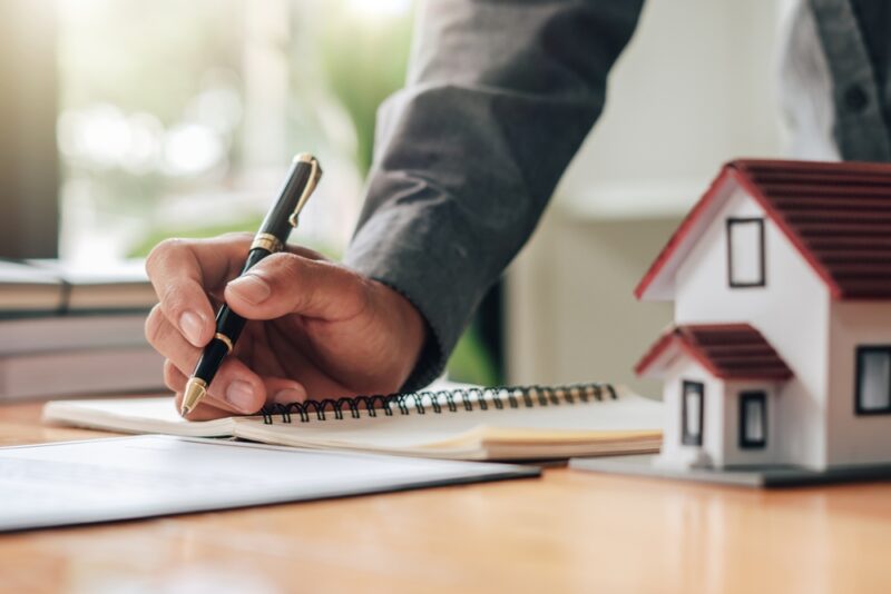 Osoba zapisuje finansijski plan pored modela kuće kao simbol procene kredita